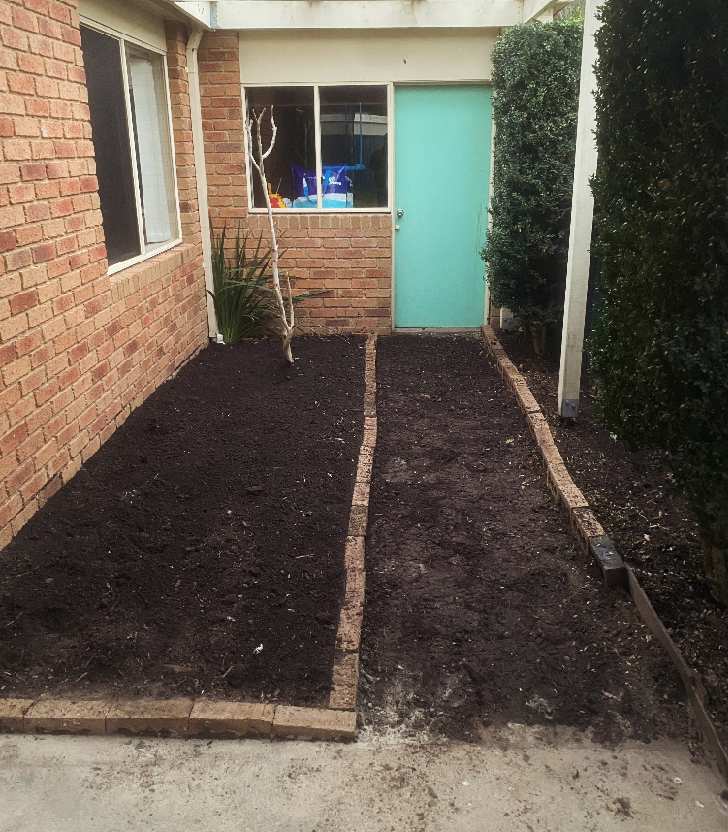 The same courtyard garden beds cleared of weeds and turned over with fresh soil, ready for planting